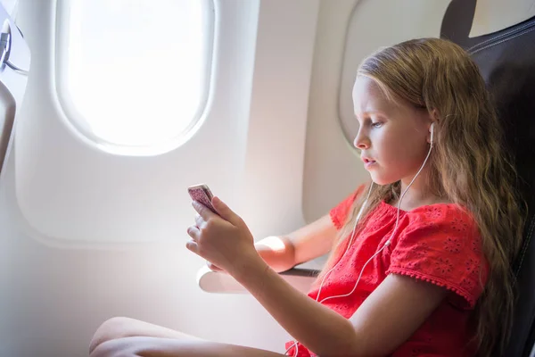 Imádnivaló kislány, aki repülővel utazik. Gyerek zenét hallgat ül közel repülőgép ablak — Stock Fotó
