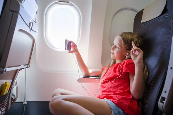 Entzückendes kleines Mädchen, das mit dem Flugzeug reist. Kind sitzt neben Flugzeugfenster — Stockfoto