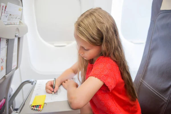 Schattig meisje reizen met een vliegtuig. Kind tekening foto met kleurrijke potloden zitten in de buurt van venster — Stockfoto