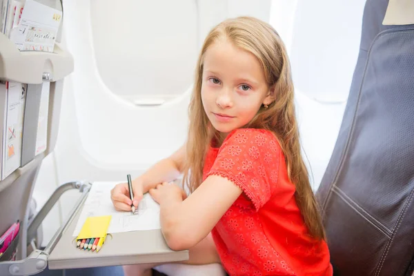 Entzückendes kleines Mädchen, das mit dem Flugzeug reist. Kind zeichnet Bild mit Buntstiften am Fenster — Stockfoto