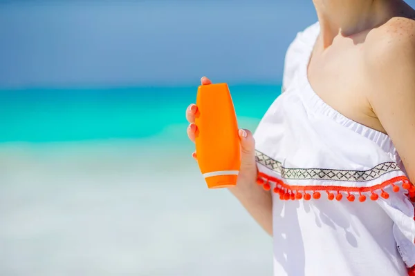 Botella de crema solar de primer plano en manos femeninas en la playa —  Fotos de Stock