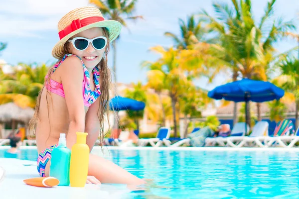 Little girl with bottle of sun cream sitting on the edge of swimming pool — Stock Photo, Image