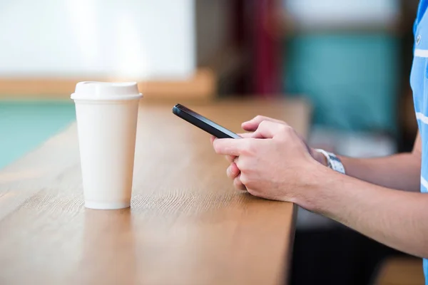 Closeup of male hands holding cellphone and glass of coffee in cafe. Man using mobile smartphone. Boy touching a screen of his smarthone.