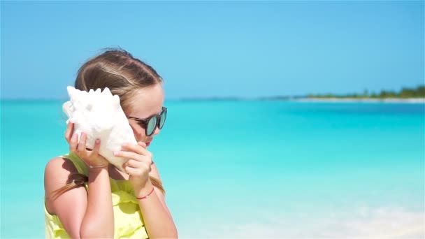 Portret van schattig meisje luisteren een grote zeeschelp op het strand. Slow motion — Stockvideo