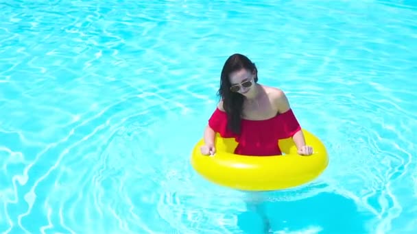 Beautiful young woman relaxing in swimming pool. Girl in outdoor pool at luxury hotel with inflatable rubber circle — Stock Video