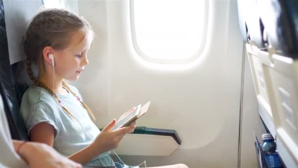 Bedårande liten flicka reser med ett flygplan. Söt unge med laptop nära fönster i flygplan — Stockvideo