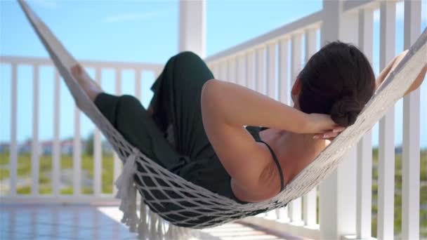 Vista trasera de la joven mujer disfrutando de un día soleado en la hamaca en su terraza — Vídeos de Stock