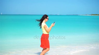 Genç bir kadın tropik plaj tatilinde telefon kullanıyor. Akıllı telefon kullanan turist.