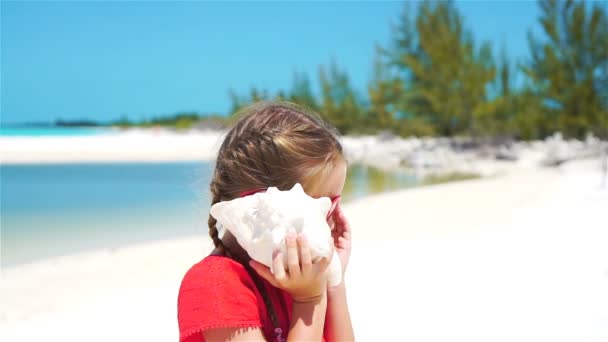 Retrato de uma menina adorável ouvindo uma grande concha na praia. LOW MOTION — Vídeo de Stock