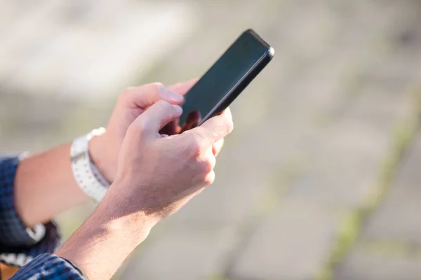 Fechamento de mãos masculinas está segurando celular ao ar livre na rua. Homem usando smartphone móvel . — Fotografia de Stock