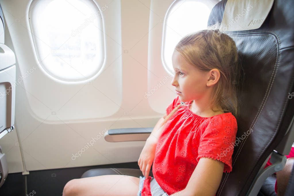 Adorable little girl traveling by an airplane. Kid sitting near aircraft window