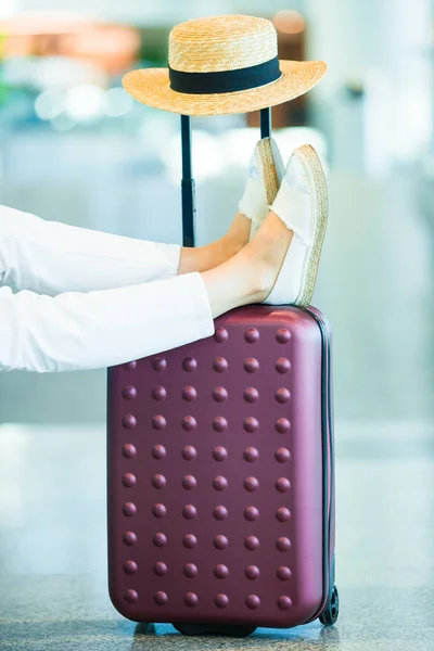 Primer plano piernas femeninas, sombrero y equipaje en el aeropuerto interior. Pasajero de aerolínea en un aeropuerto esperando aviones de vuelo —  Fotos de Stock