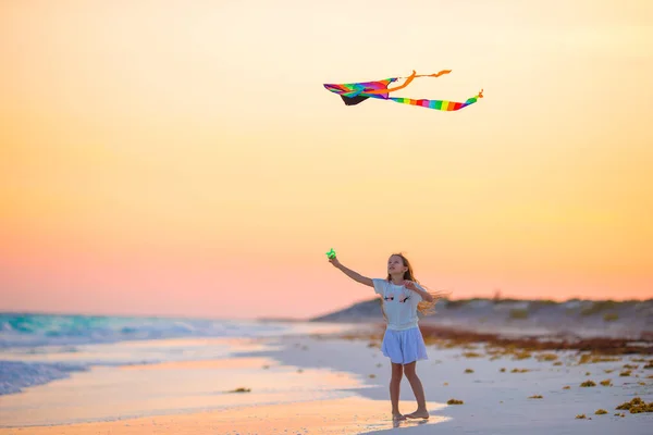 Holčička s létání draka na tropické pláži při západu slunce. Kid hrát na břehu oceánu. Dítě s plážové hračky. — Stock fotografie