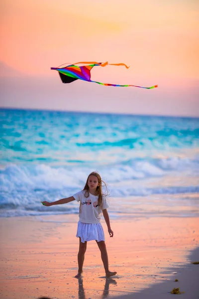 Petite fille avec cerf-volant volant sur la plage tropicale au coucher du soleil. Enfant jouer sur la côte de l'océan avec des jouets de plage . — Photo