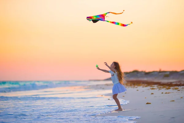 Kleines Mädchen mit fliegendem Drachen am tropischen Strand bei Sonnenuntergang. Kinder spielen an der Küste. Kind mit Strandspielzeug. — Stockfoto