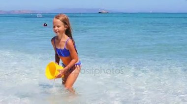 Sevimli küçük kız var eğlenceli plaj oyuncakları sığ suda ile tropikal plaj