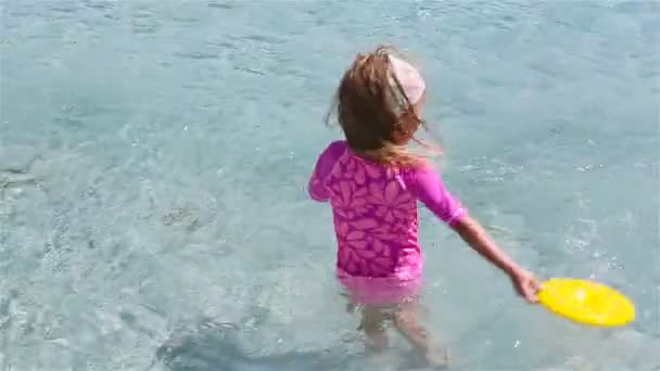 Niña adorable jugando frisbee durante las vacaciones tropicales. Niño divertirse con juguete de playa en aguas poco profundas — Vídeo de stock
