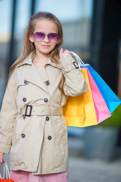 Retrato de niña adorable con bolsas de compras al aire libre. Niño de moda en la ciudad europea al aire libre — Foto de Stock