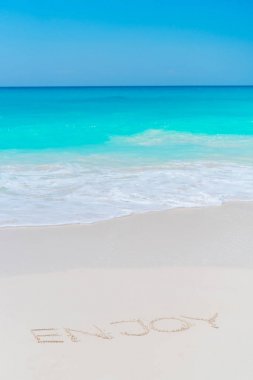 Turkuaz su ile kum plajındaki el yazısıyla yazılmış kelime keyfini çıkarın