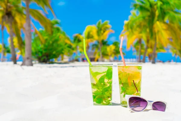 Two cold tasty mohito cocktails and white sunglasses on the white sandy beach — Stock Photo, Image