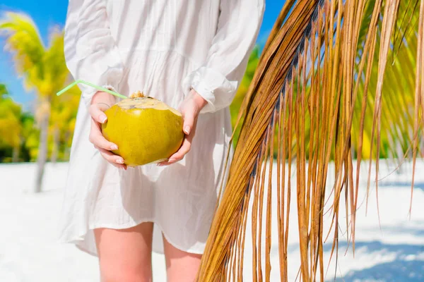 Mujer joven bebiendo leche de coco en un día caluroso en la playa. Coco de cerca en manos femeninas cerca de la palmera —  Fotos de Stock