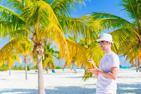 Młody mężczyzna picia mleka kokosowego na upalny dzień na plaży w palm grove — Zdjęcie stockowe