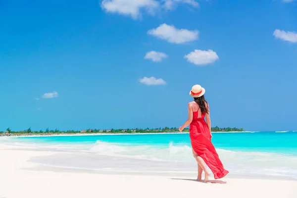 Joven mujer hermosa en la orilla del mar tropical. Vista posterior de la joven en vestido rojo fondo el mar — Foto de Stock