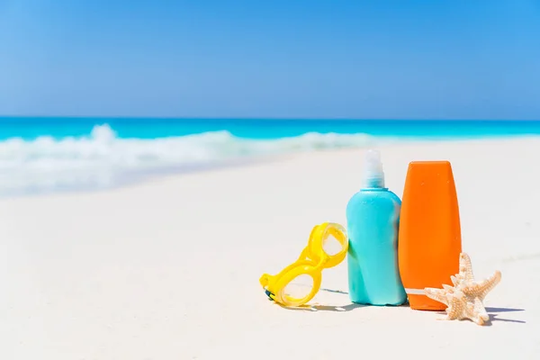 Zonnebrandcrème flessen, bril, zeester op wit zand strand achtergrond Oceaan — Stockfoto