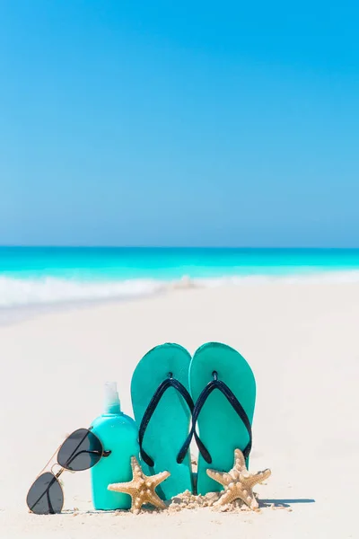 Opalovací krém láhev, flip flops, hvězdice a sluneční brýle na bílém písku beach pozadí oceánu — Stock fotografie