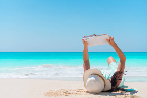 Young woman reading book lying tropical white beach