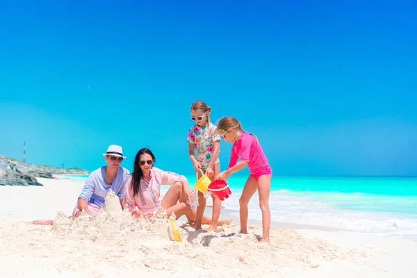 Rodina se dvěma dětmi dělat hrad z písku na tropické pláži — Stock fotografie