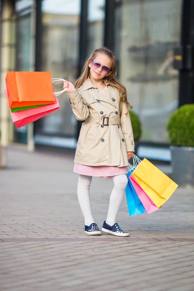 Adorable little girl walking with shopping bags outdoors in Europe. Fashion toddler kid in european city outdoors — Stock Photo, Image