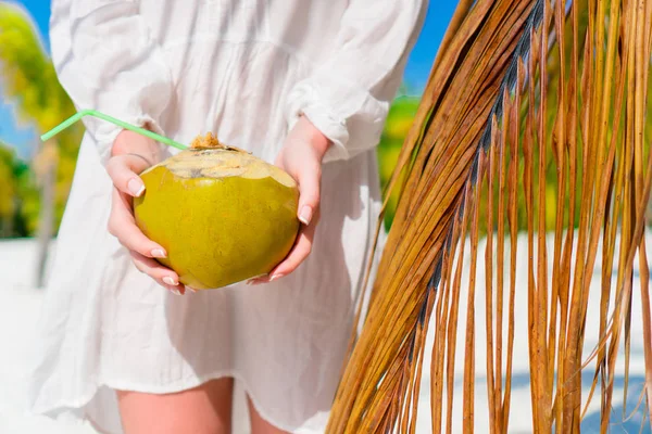 Young woman drinking coconut milk on hot day on the beach. Close-up coconut in female hands near palmtree — Stock Photo, Image