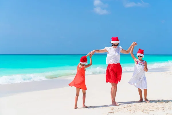 Happy beautiful family in red Santa hats on a tropical beach celebrating Christmas — Stock Photo, Image