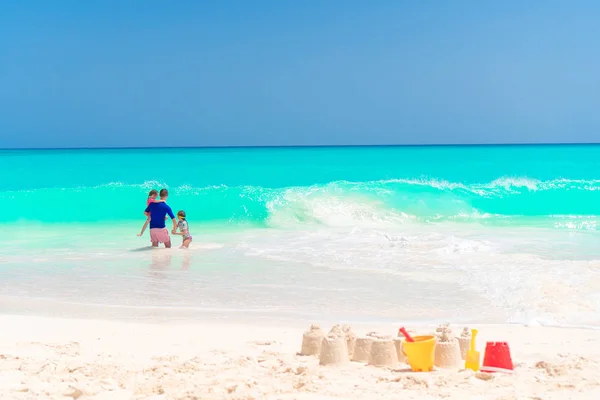 Песчаный замок на белом пляже с пластиковыми игрушками и морским фоном — стоковое фото