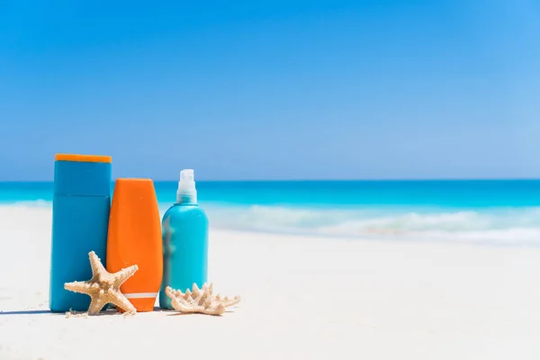 Opalovací krém láhve, brýle, hvězdice na bílé písčité pláži pozadí oceánu — Stock fotografie