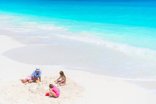 Отец и маленькие дочери строят замок из песка на тропическом пляже — стоковое фото