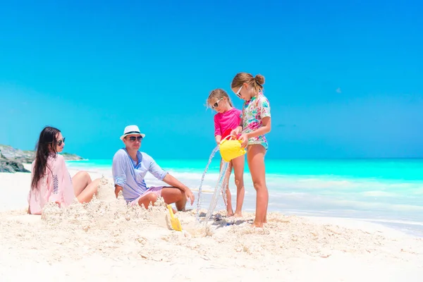Семья с двумя детьми строит песчаный замок на тропическом пляже — стоковое фото