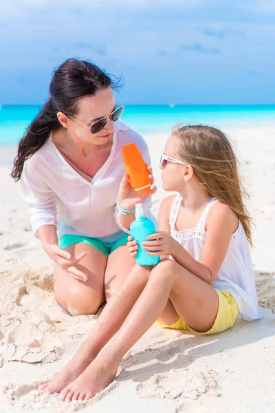 Заботливая мама наносит солнцезащитный крем ребенку на белый пляж. Концепция защиты от ультрафиолетового излучения — стоковое фото