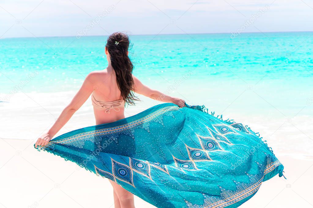 Beautiful bikini body woman relaxing in flowing cover-up beachwear fashion wrap on ocean sunset background.
