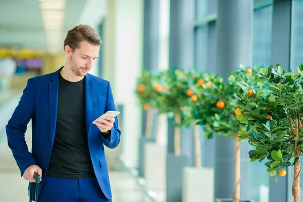 Człowiek z inteligentny telefon wewnątrz w Lotnisko. Dorywczo młody chłopak sobie garnitur marynarka. Kaukaski mężczyzna z telefonu komórkowego na lotnisku w oczekiwaniu na wejście na pokład — Zdjęcie stockowe