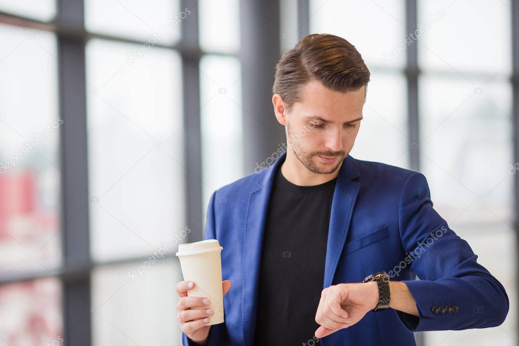 Urban man with coffee inside in airport. Casual young boy wearing suit jacket. Caucasian man with cellphone at the airport while waiting for boarding