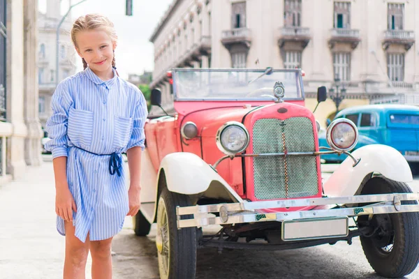 Urocza dziewczynka w popularnej dzielnicy w starej Hawanie. Portret dziecko tło vintage klasyczny amerykański samochód — Zdjęcie stockowe