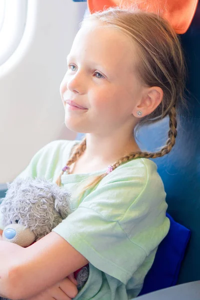 Entzückendes kleines Mädchen, das mit dem Flugzeug reist. Kind sitzt mit Teddybär am Flugzeugfenster — Stockfoto