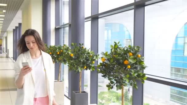 Young woman with smartphone in international airport. Airline passenger in an airport lounge waiting for flight aircraft — Stock Video