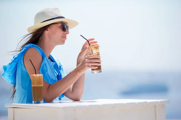 Chica joven bebiendo café frío disfrutando de vistas al mar. Hermosa mujer relajarse durante vacaciones exóticas en la playa disfrutando de frappe — Foto de Stock
