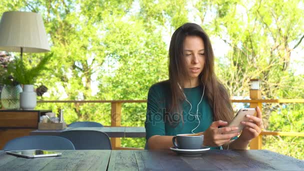 Mujer con teléfono inteligente en la cafetería bebiendo café sonriendo y mensajes de texto en el teléfono móvil. Retrato de una hermosa joven — Vídeos de Stock