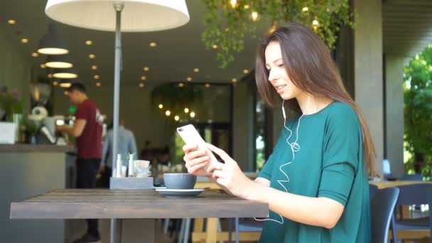 自由時間中に喫茶店で一人で座っている間携帯電話で呼び出して若い魅力的な女性 — ストック動画