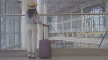 Uluslararası havaalanında bavuluyla yürüyen bagajlı genç bir kadın. Havaalanı lobisindeki yolcu uçuş için bekliyor.