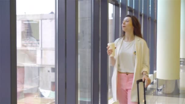 Egy fiatal nő poggyásszal a nemzetközi repülőtéren, aki a csomagjaival sétál. Légitársaság utas egy repülőtéri társalgóban várja a repülőgépet — Stock videók